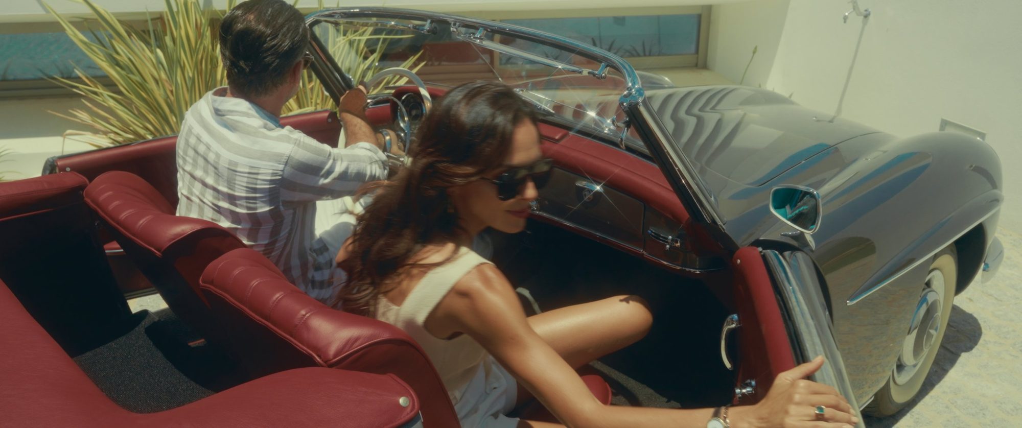 A woman in sunglasses steps into a red-upholstered convertible