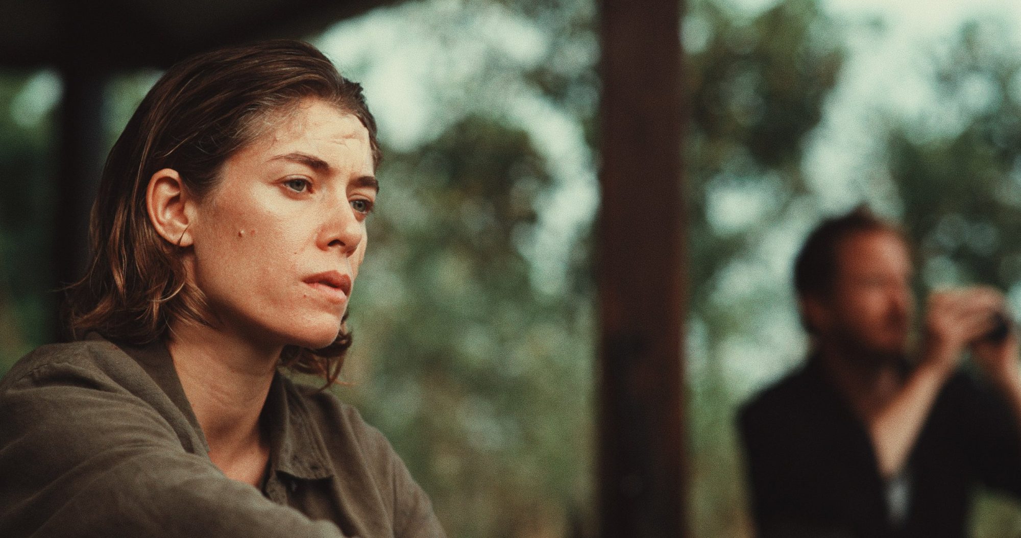 A woman in soft daylight, a man with binoculars behind her