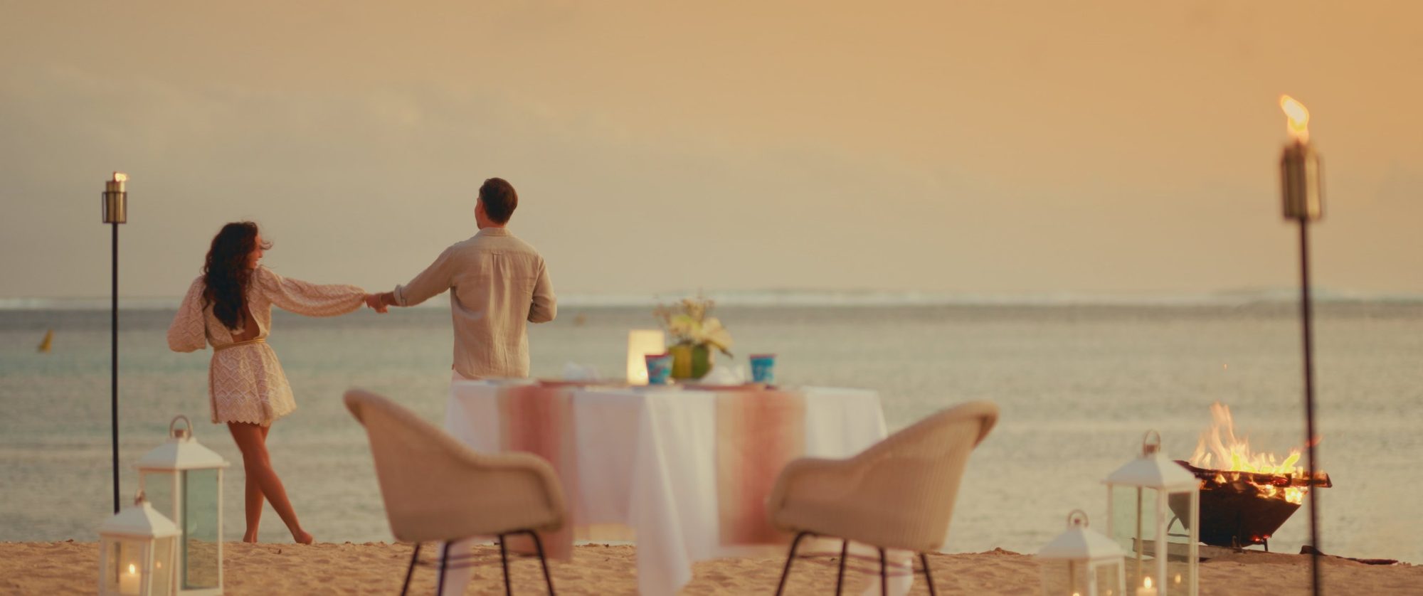 A couple dances past a candlelit beach dinner at golden hour