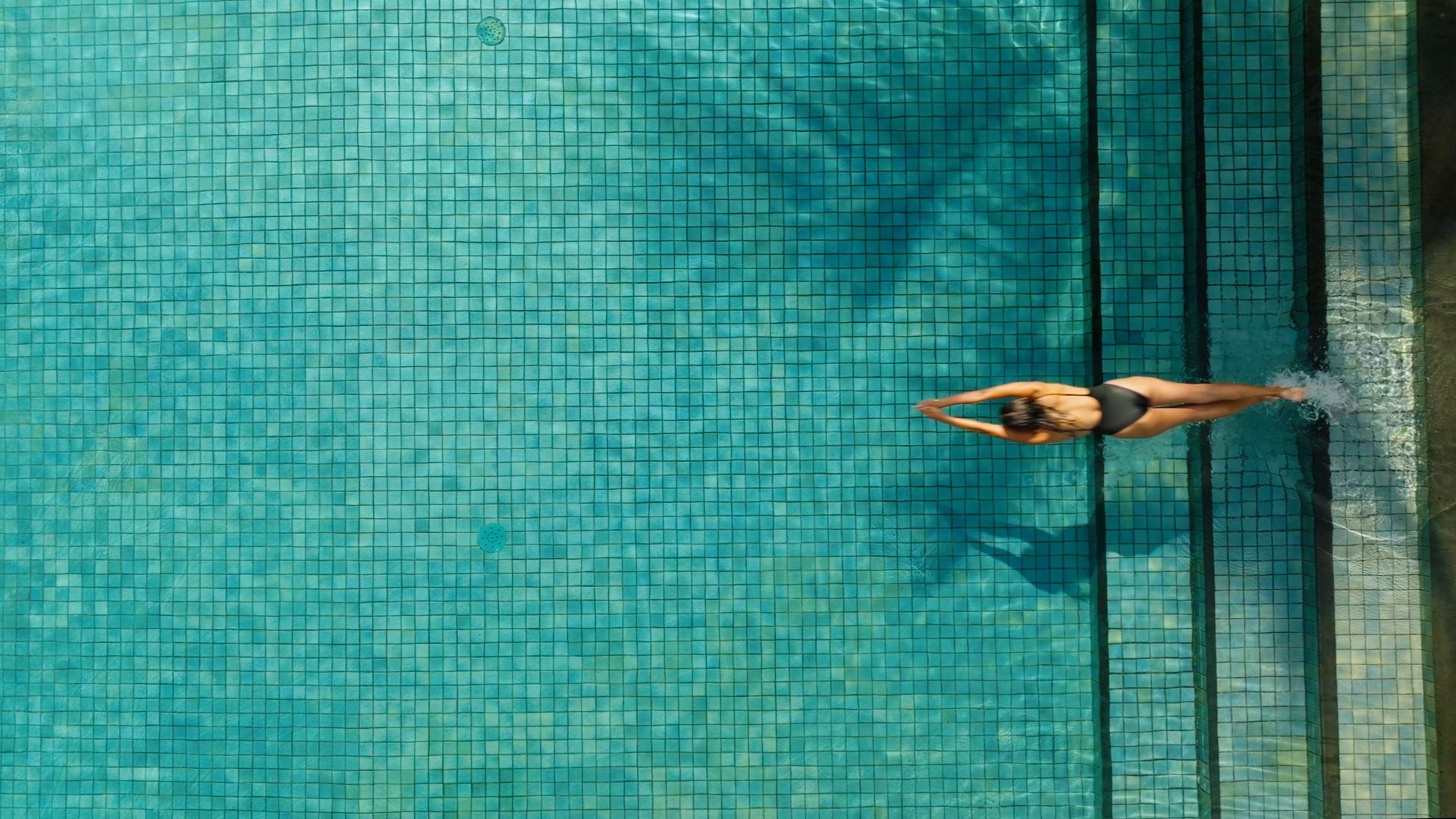 Aerial: a swimmer glides off the steps of a green-tiled pool