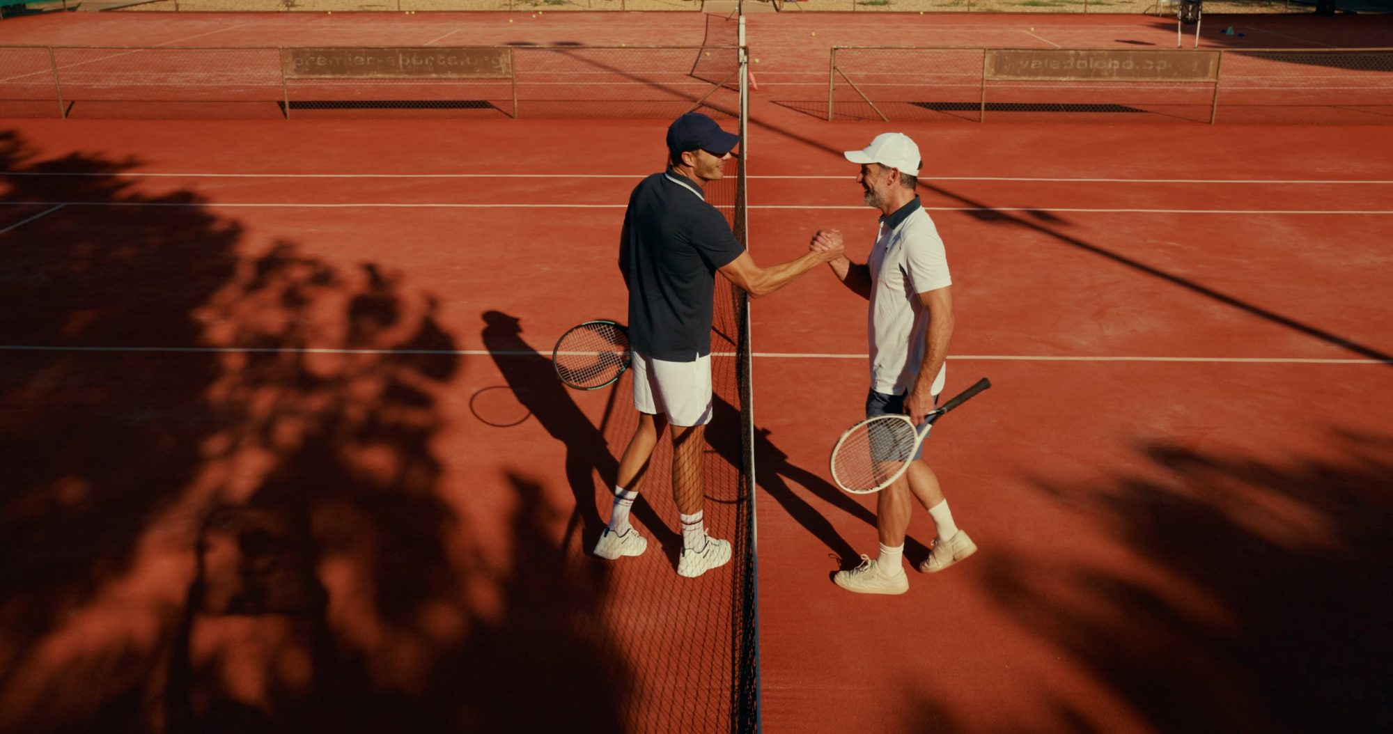 Two tennis players shake hands over the net on a clay court