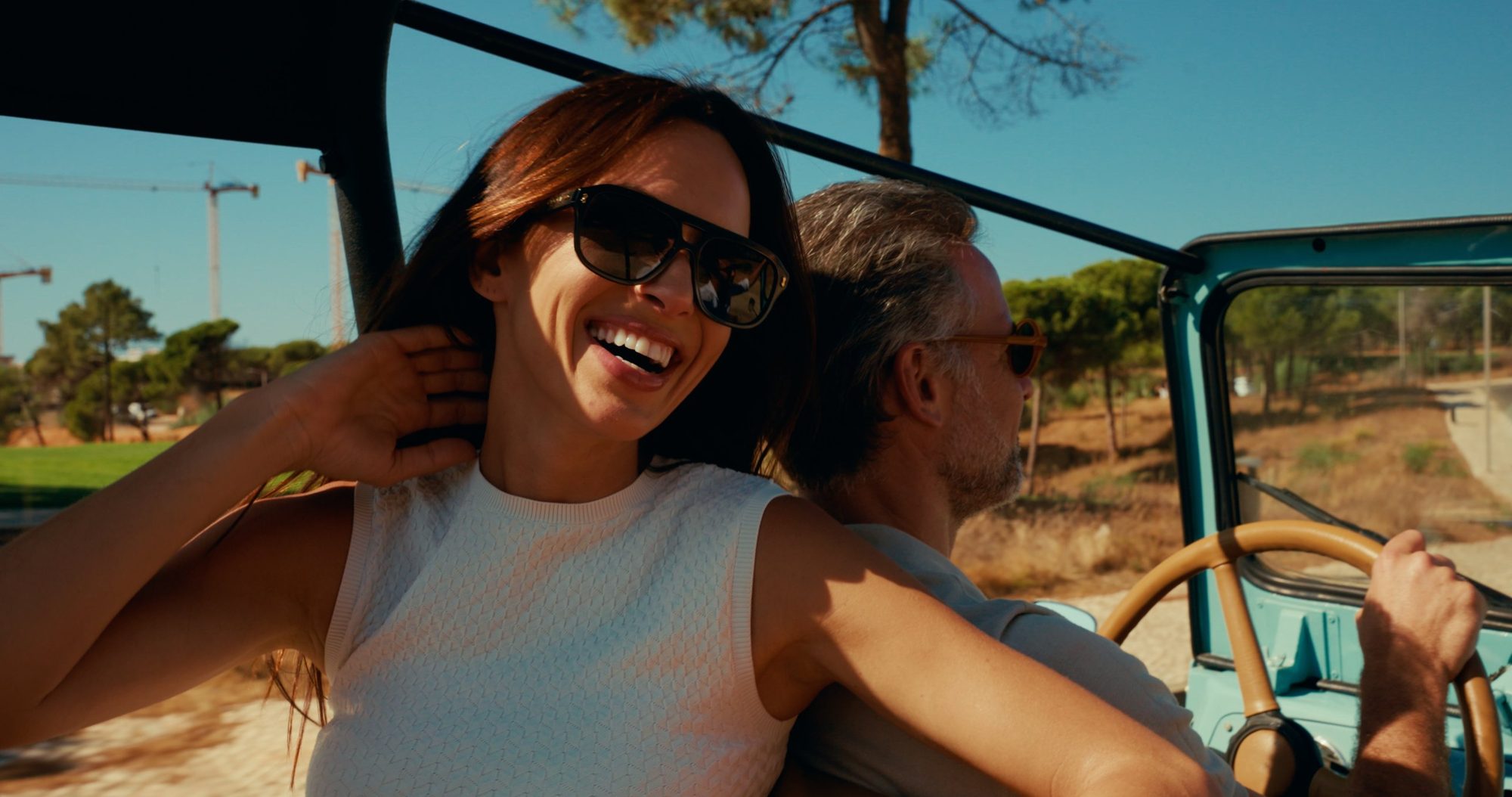 A woman laughs in the passenger seat of an open blue jeep