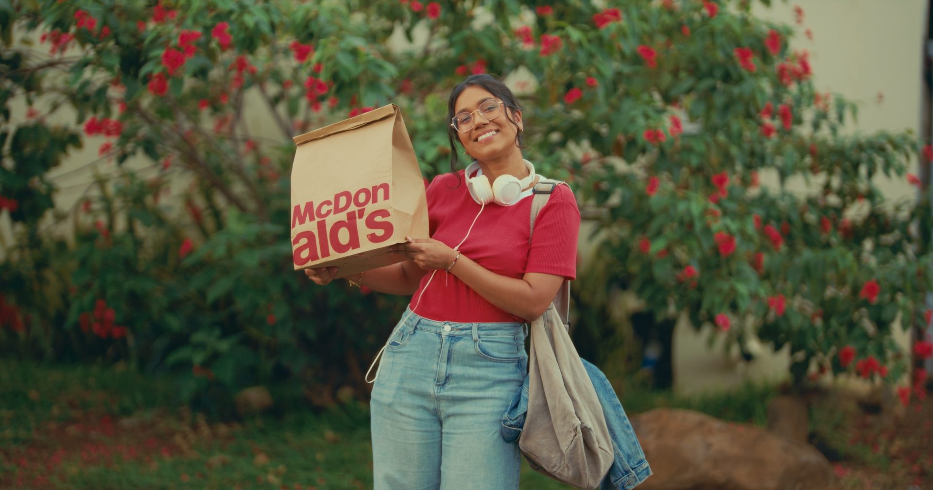 A smiling student holds up a McDonald's bag in front of a flowering tree