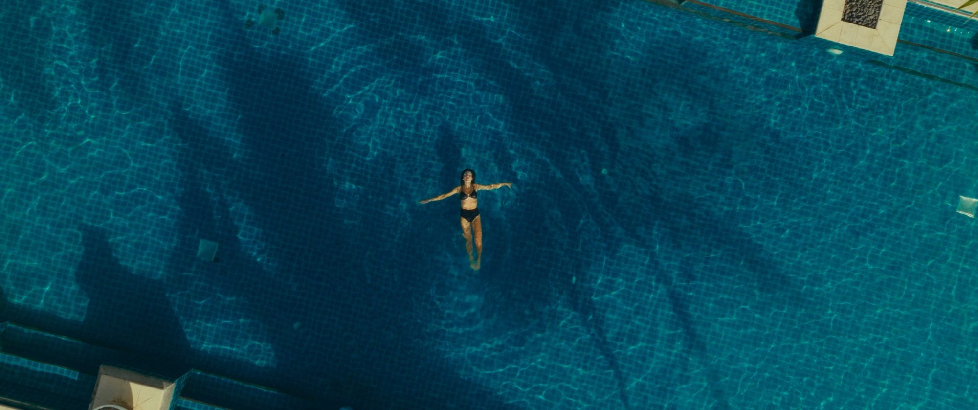 Aerial: a woman floats alone in a deep blue pool